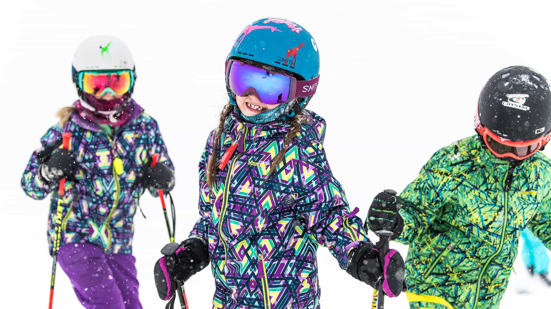 three children skiers pose, with the one in the middle smiling widely.