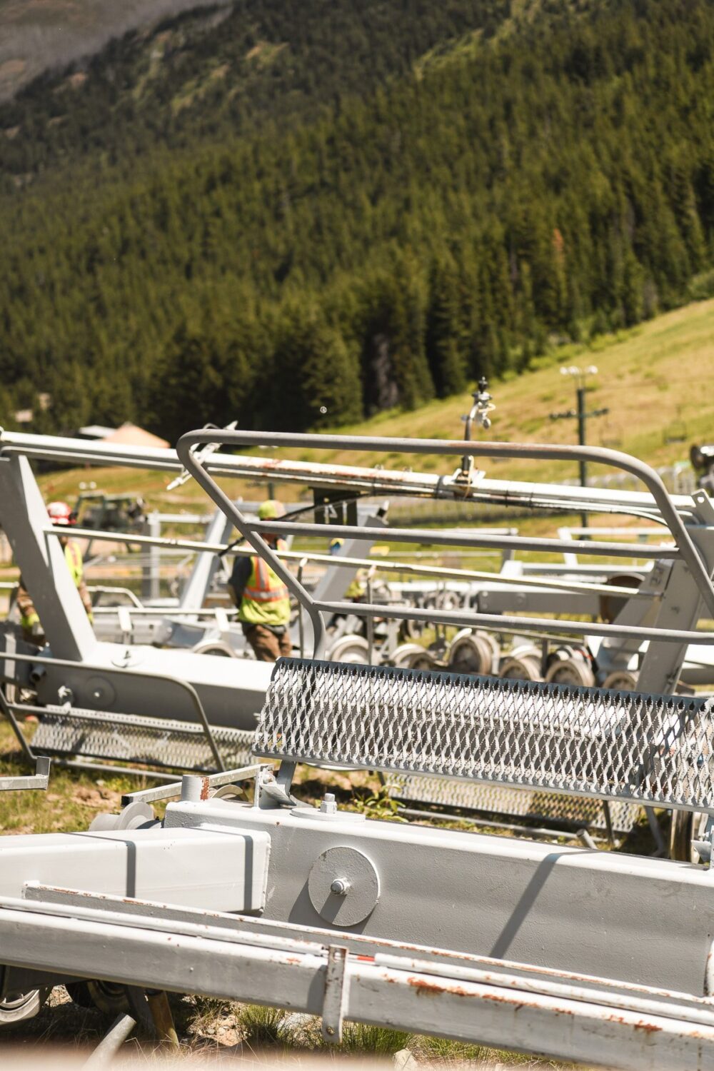 Construction crew working on Crystal Mountain ski lift components during off-season maintenance, with metal frames and rollers in the foreground and grassy slopes in the background.