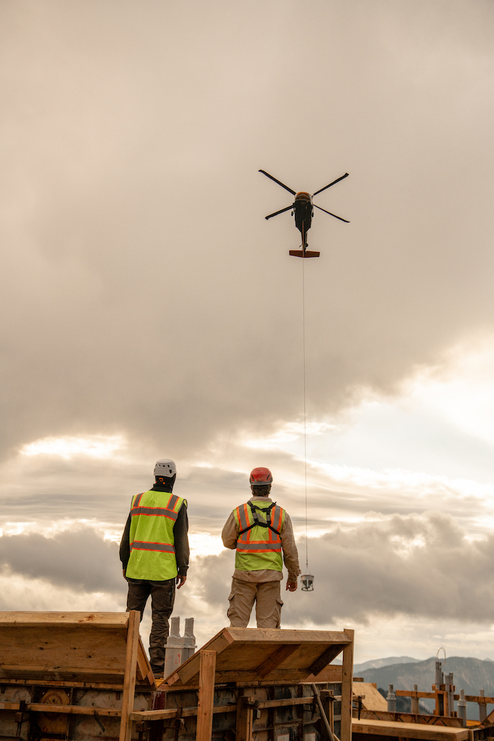 Two workers stare up at a helicopter and wait for the first bucket to touch down.
