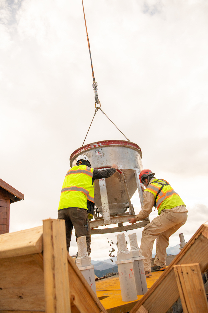 Two workers steady the concrete bucket as a helicopter lowers it.