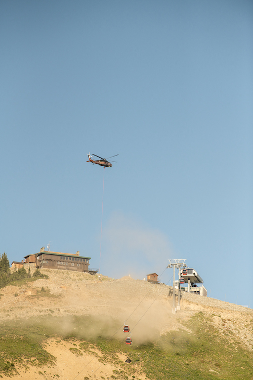 Helicopter flies above a mountain peak attempting a rotor wash.