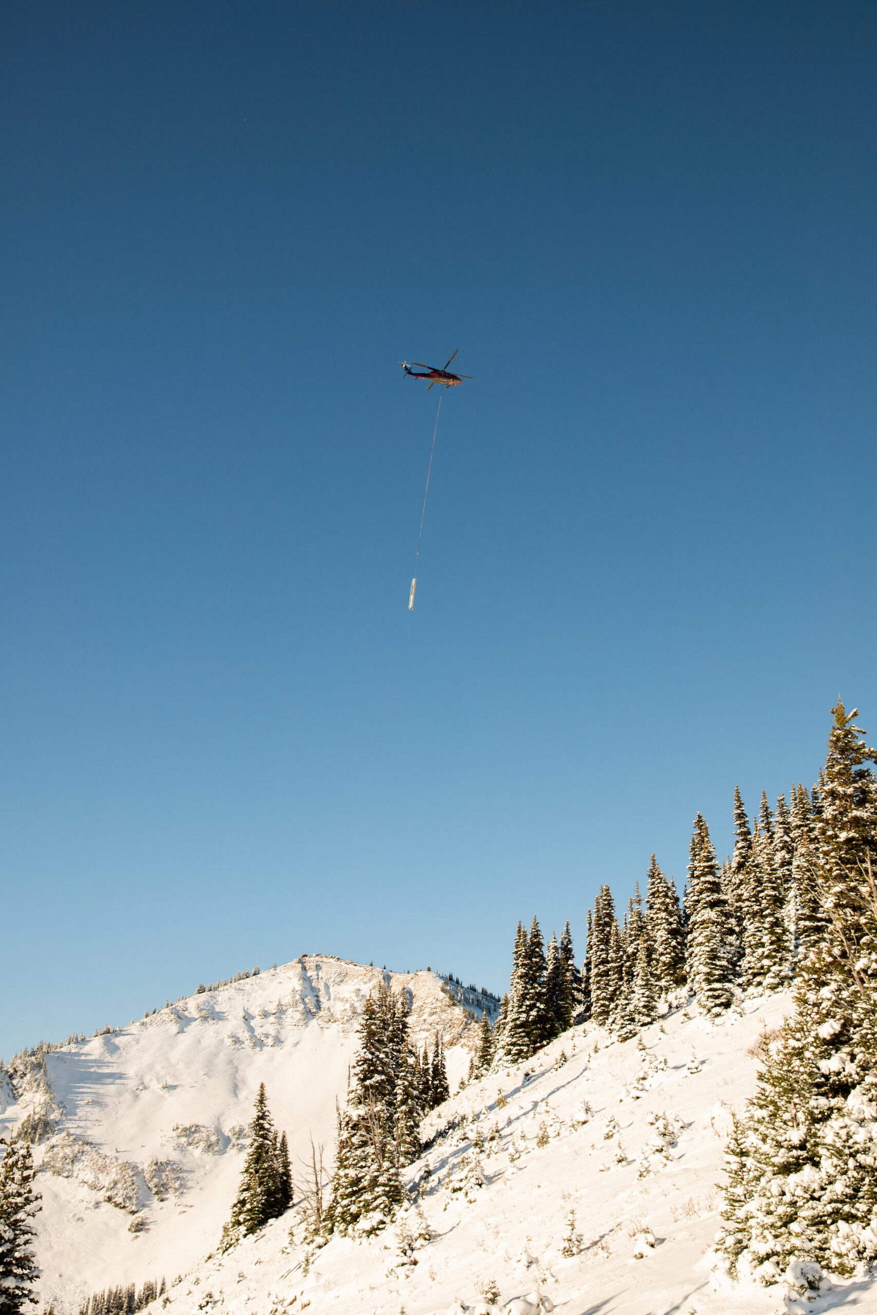 A helicopter flies above a mountain ridge on a sunny day.