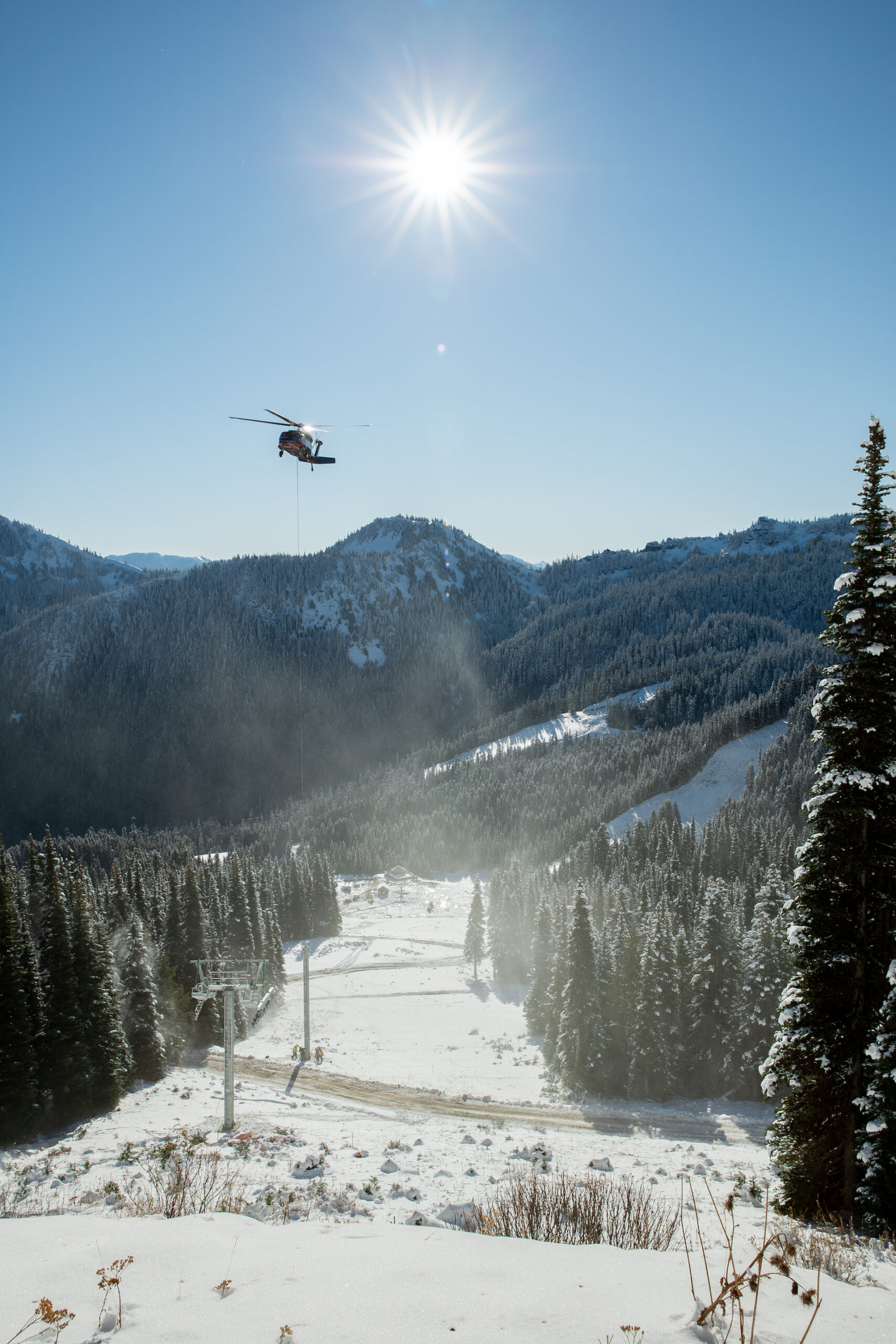 A snowy ski run lies underneath a blue sky on a sunny day with a helicopter in the background.