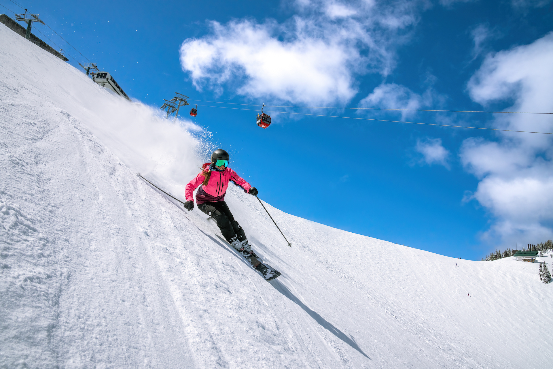 Woman skier in pink ski jacket smiles as she makes an excellent turn