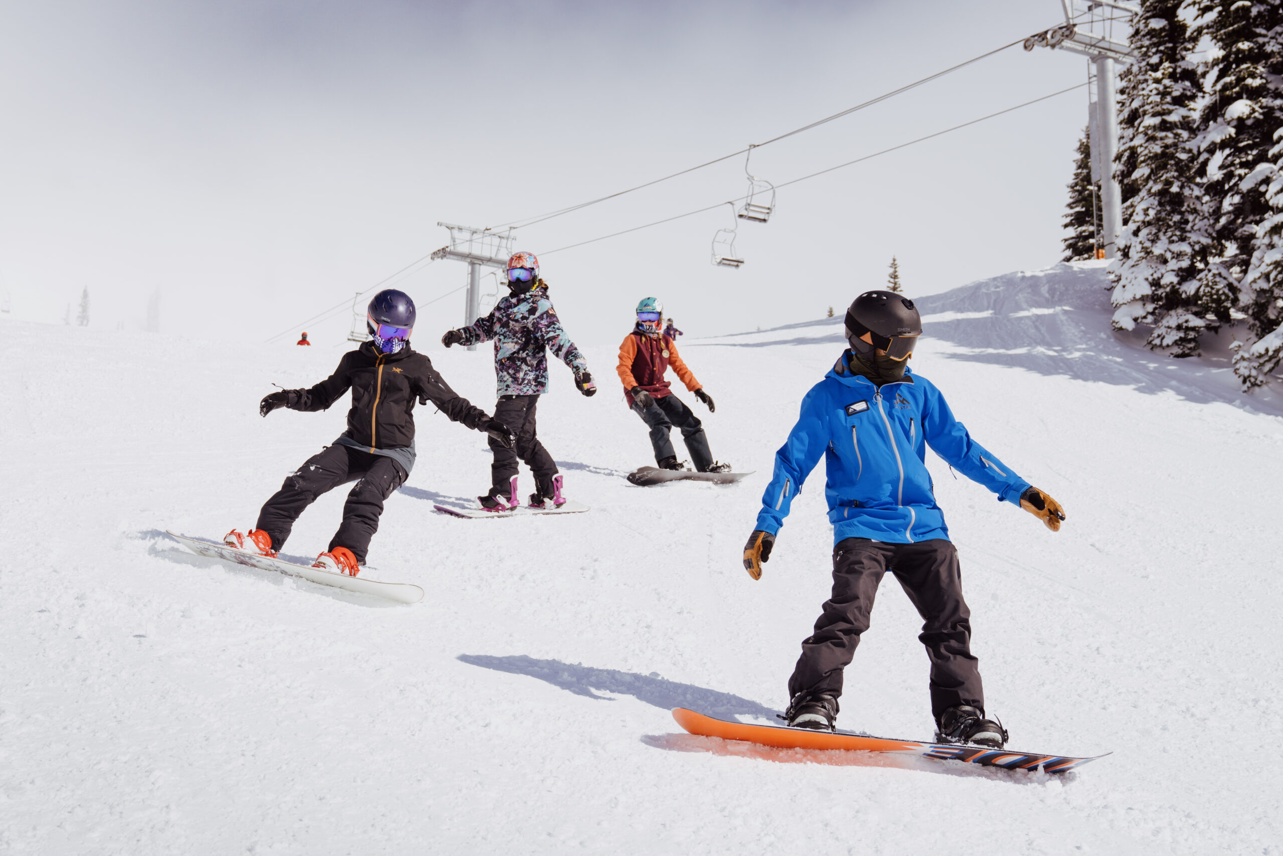 First-time snowboarders following their instructor closely down the mountain