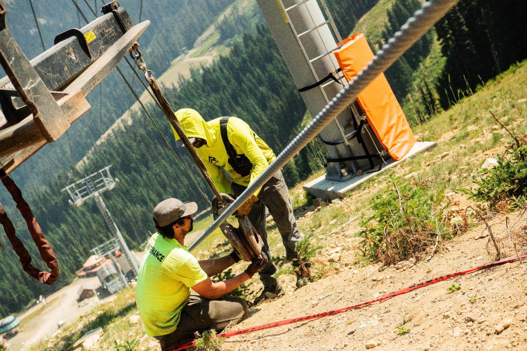 two maintenance workers work to fix a pole to a larger device.